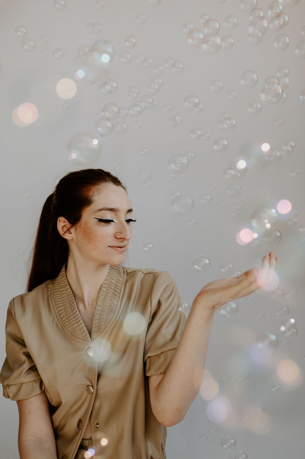 Whimsical portrait with floating soap bubbles against light background.