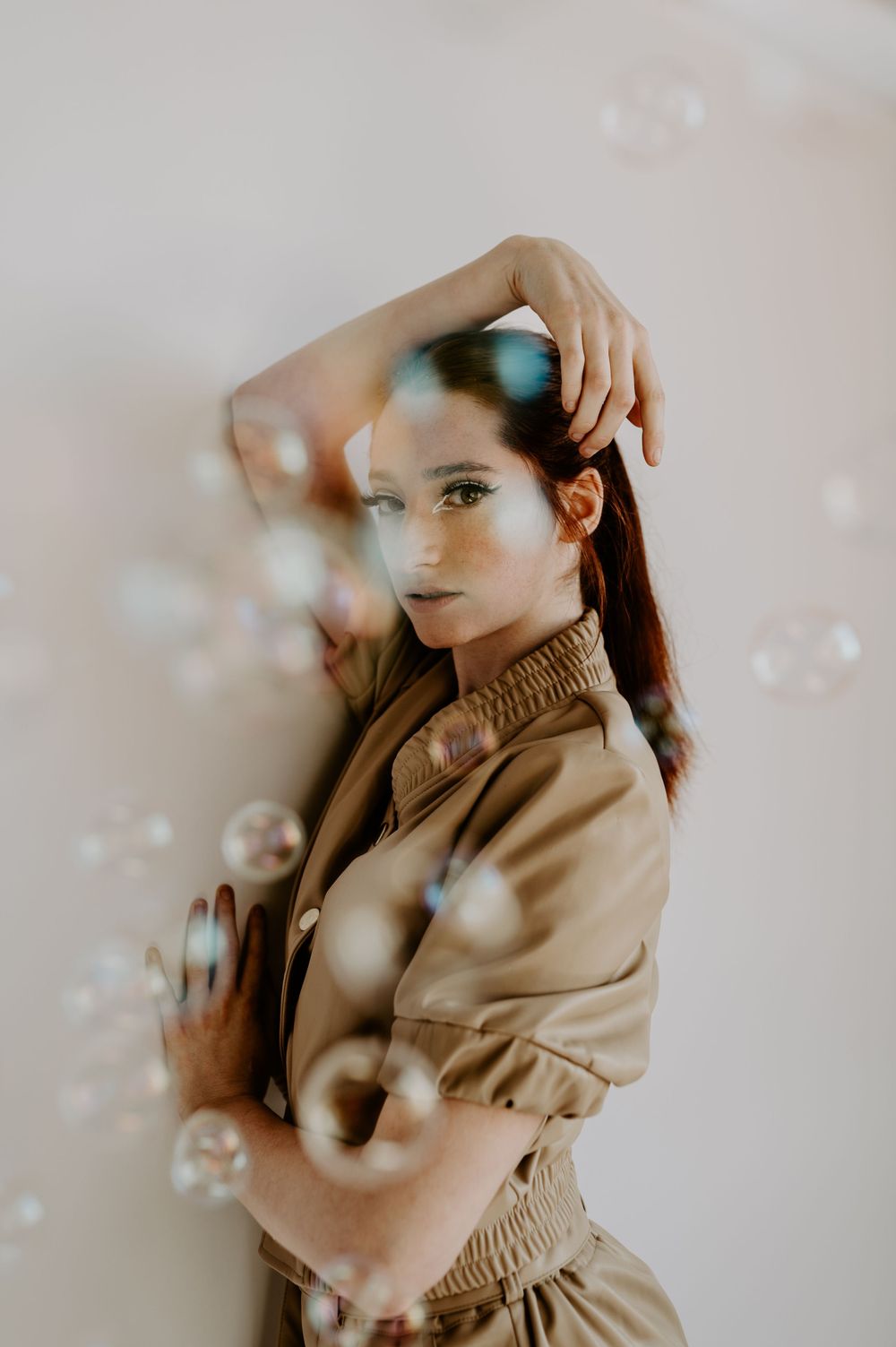 Artistic portrait with soap bubbles and soft lighting in beige tones.