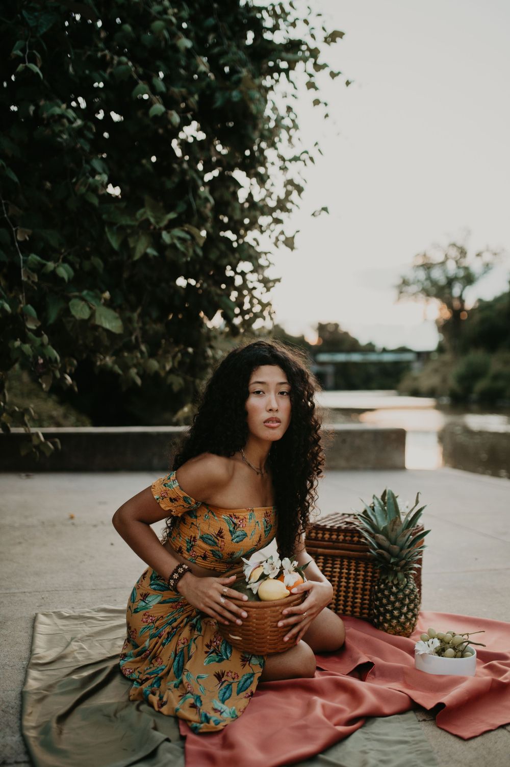 A summer picnic scene with a floral dress, fresh fruit, and a woven basket on a coral blanket.