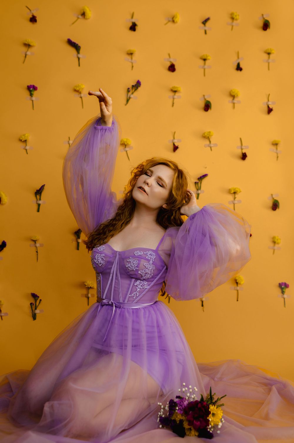 Ethereal portrait in lavender tulle dress against yellow wall with floating flowers.