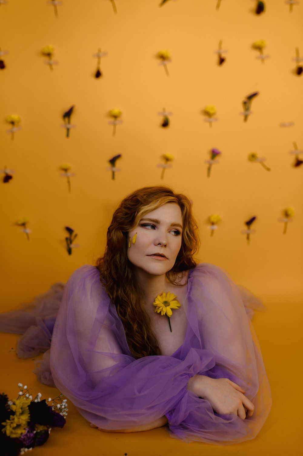 Dreamy portrait with purple gown against yellow background with suspended flowers.