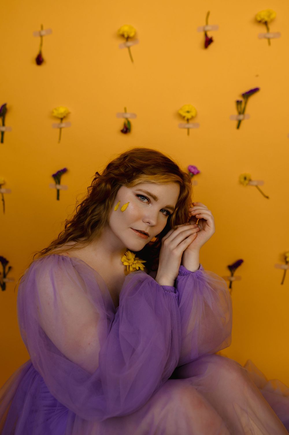 Whimsical fashion portrait in purple tulle dress against floral wall backdrop.