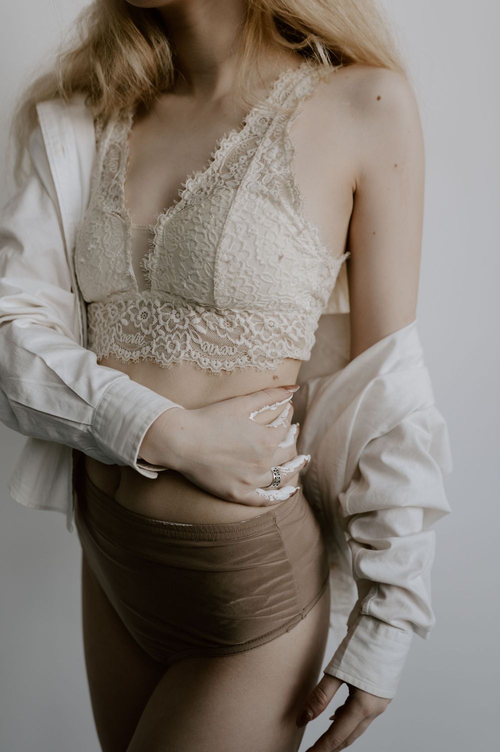 Close-up fashion detail of lace bralette and brown high-waisted bottoms with white button-down.