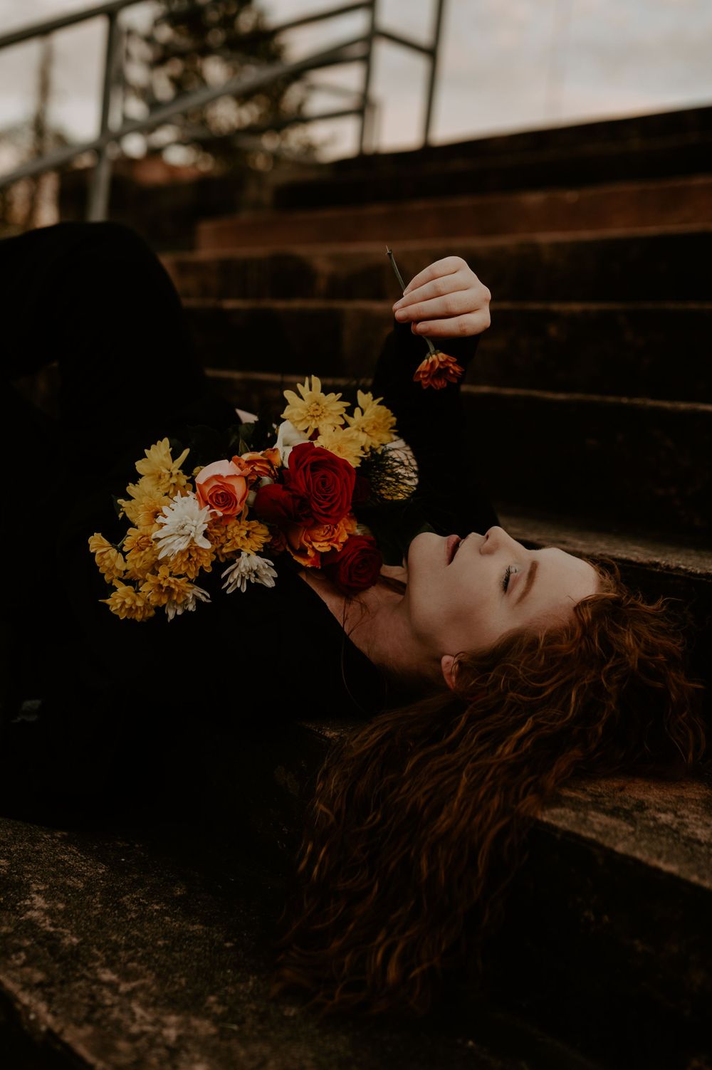 Moody portrait of woman lying on steps with colorful bouquet of flowers.