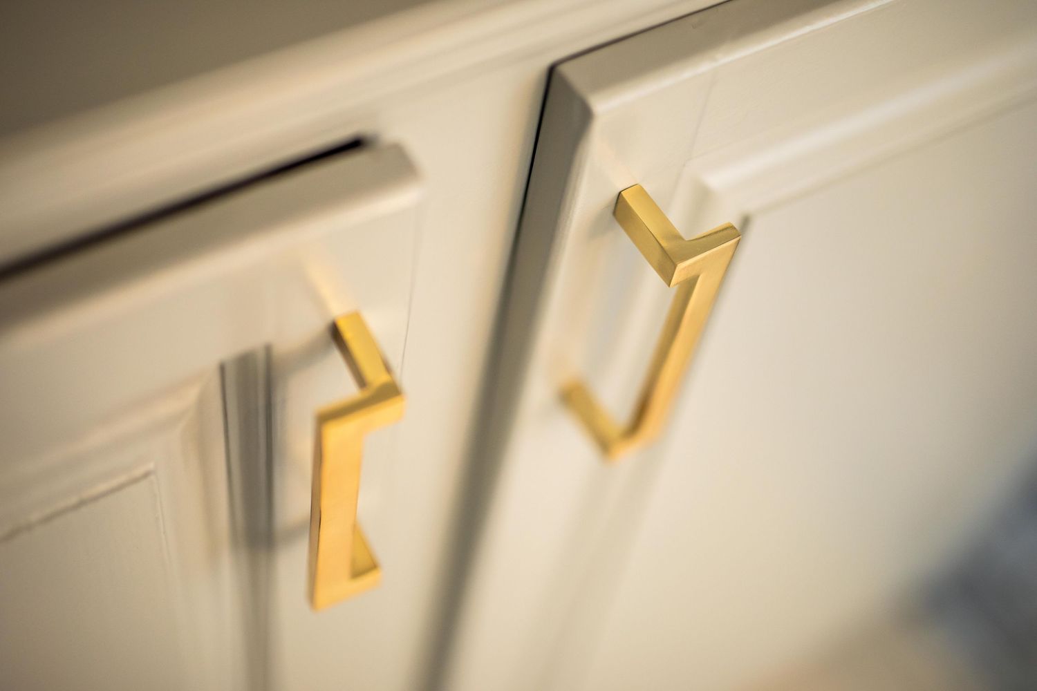 Close-up of gold modern cabinet handles on white cabinets.