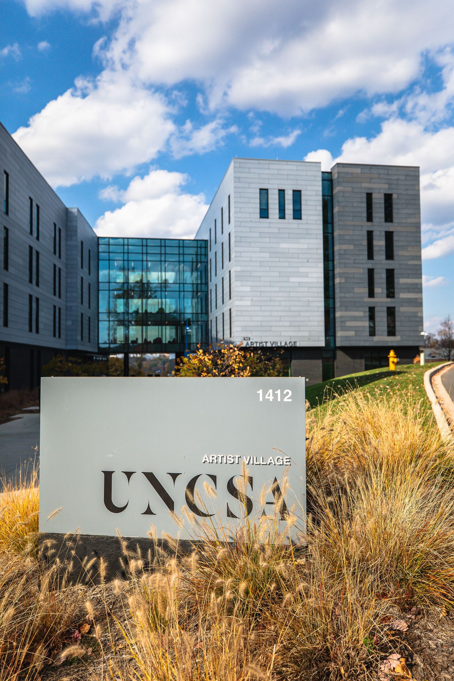 Modern UNCSA campus building exterior with sign and contemporary architecture against blue sky.