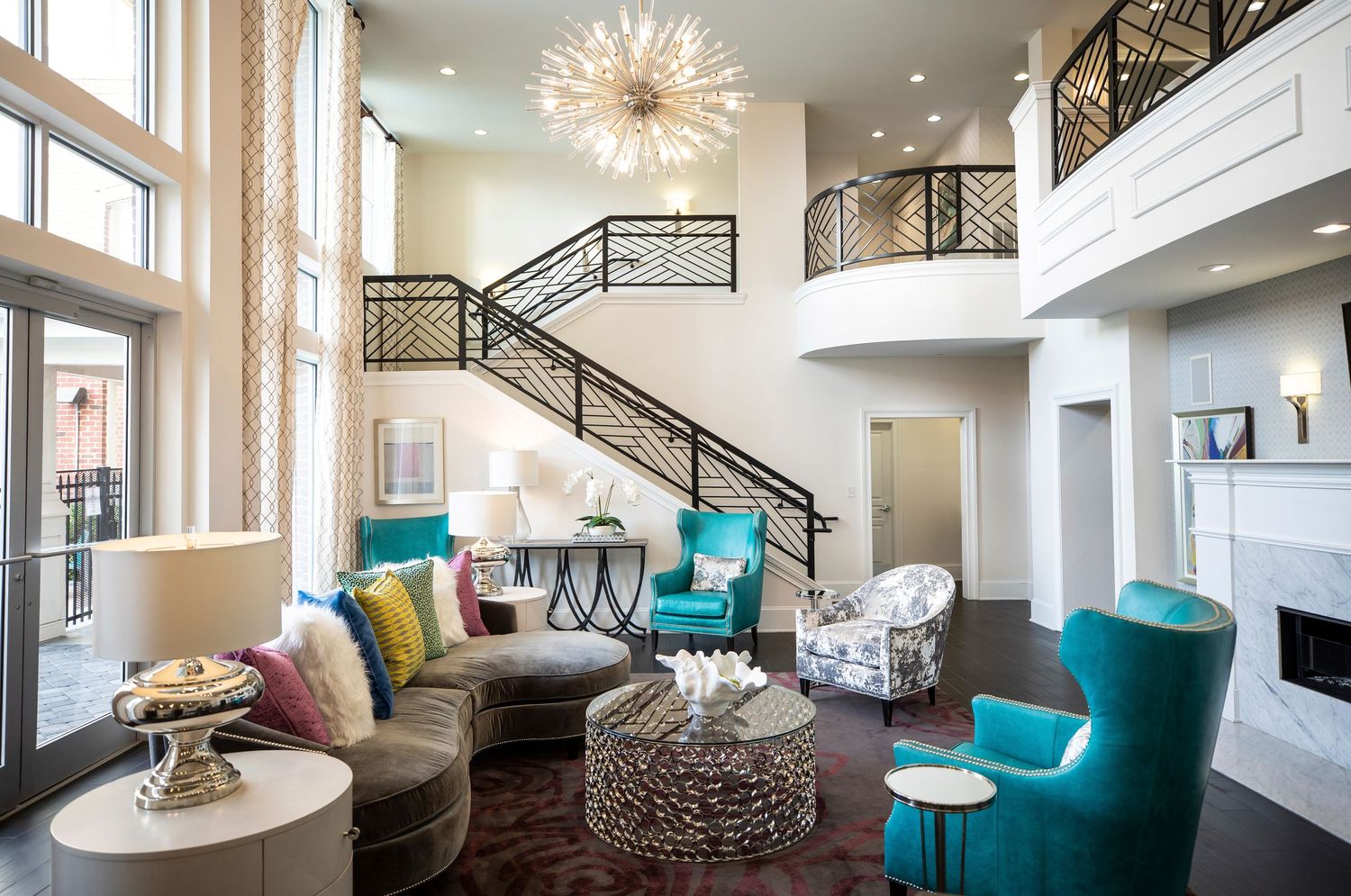Luxury living room with spiral staircase, turquoise accent chairs and statement chandelier.
