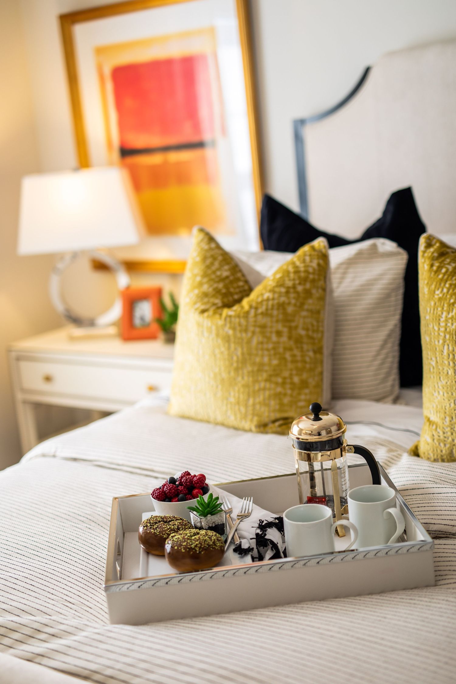 Breakfast tray with pastries and coffee on white bed with yellow accent pillows.