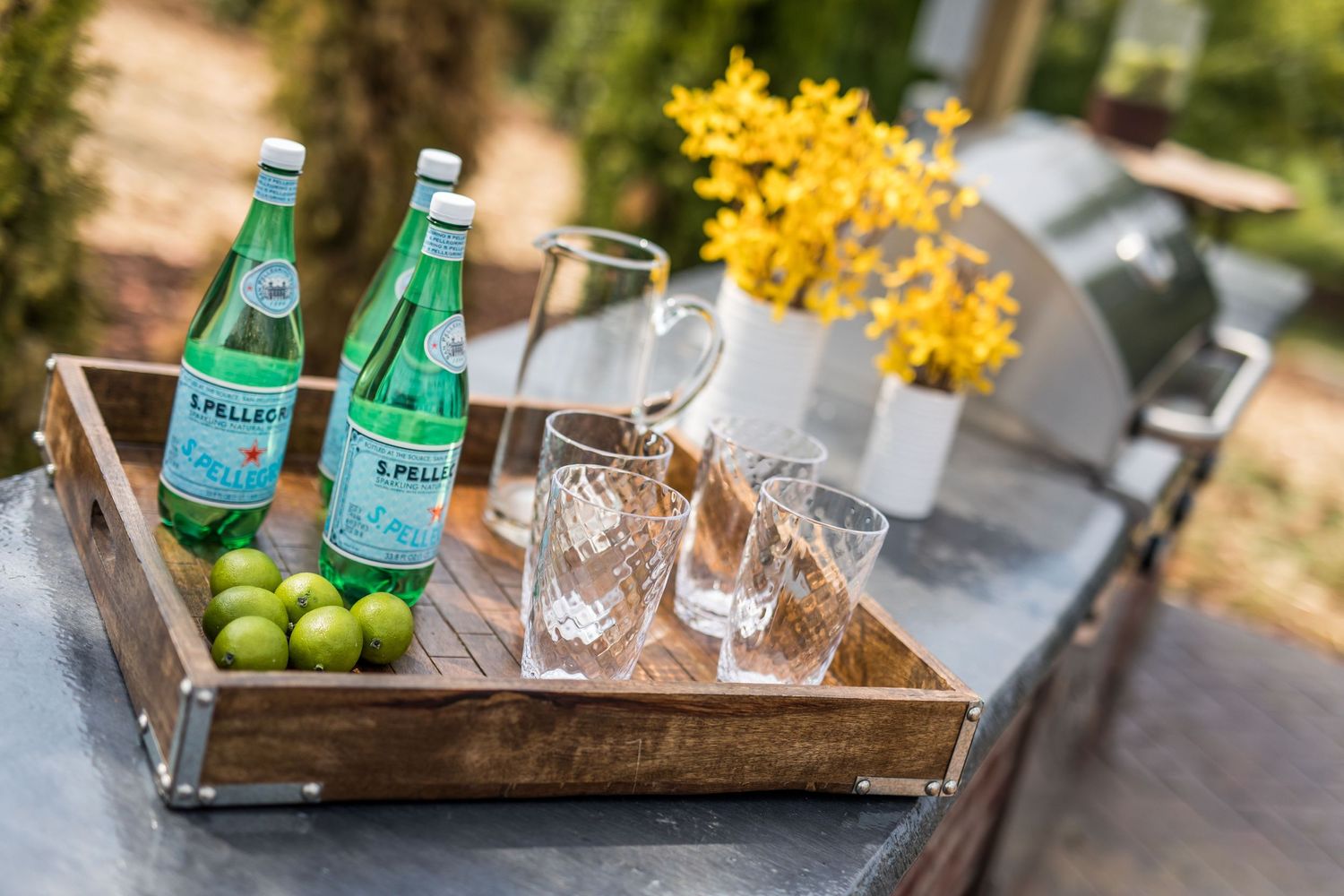 Wooden serving tray with Sprite bottles, limes and glasses on outdoor table.