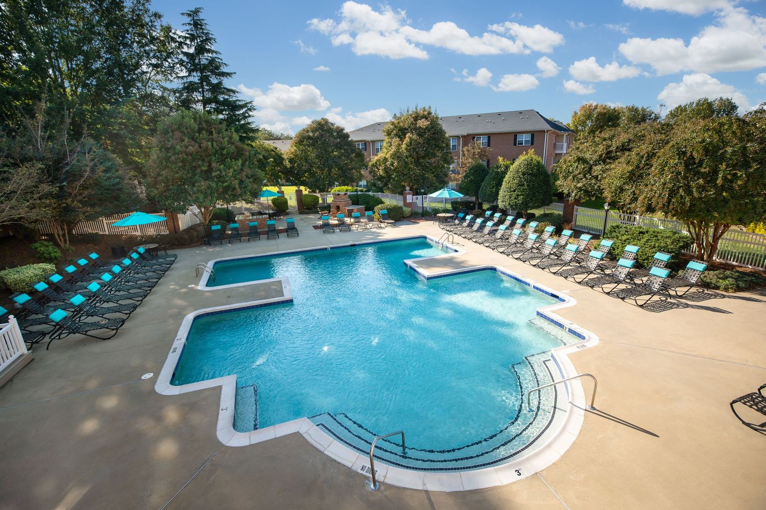 Resort-style swimming pool with lounge chairs and blue umbrellas surrounded by lush landscaping.