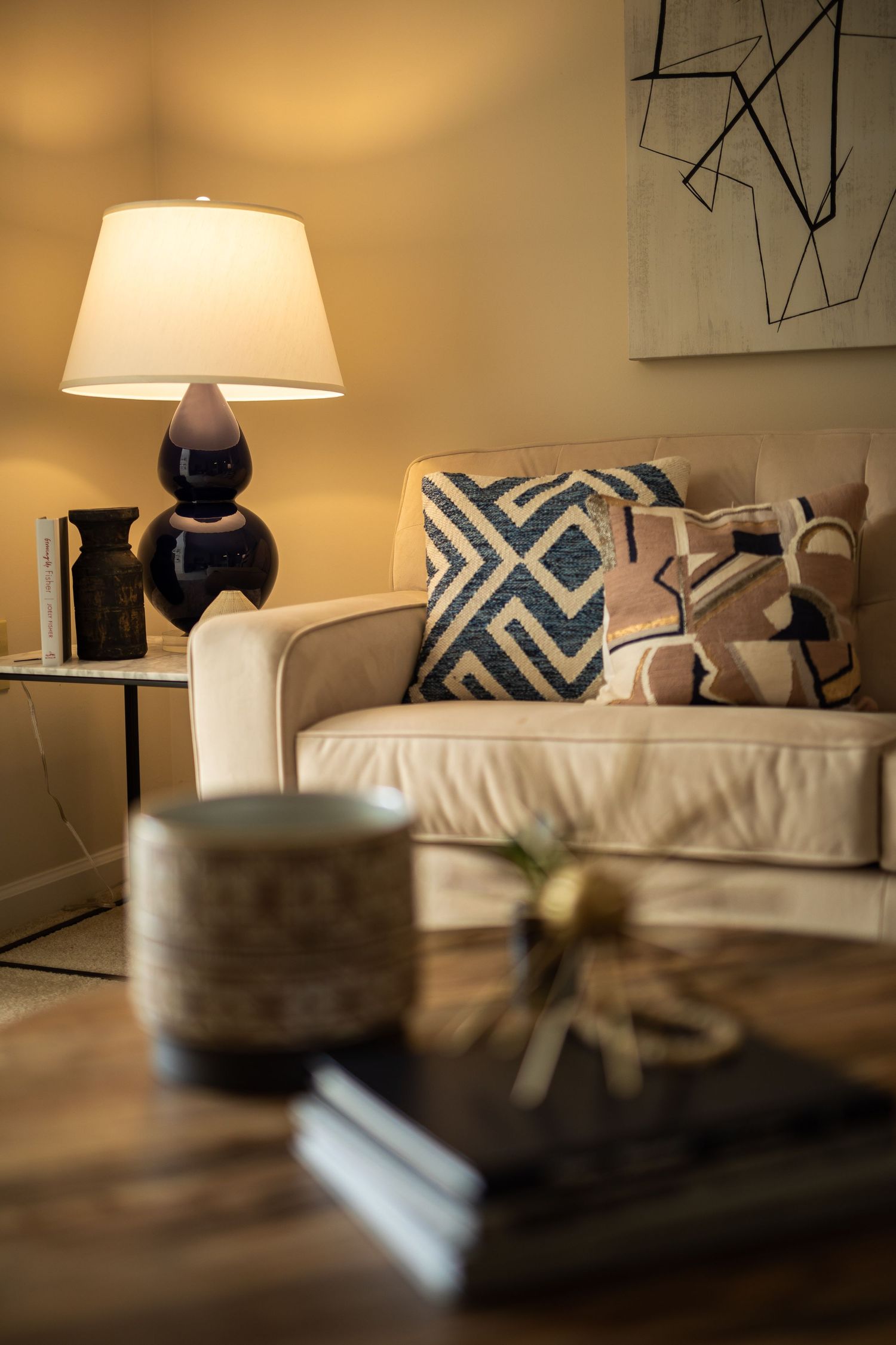 Cozy living room corner with navy lamp, geometric pillows and beige sofa.
