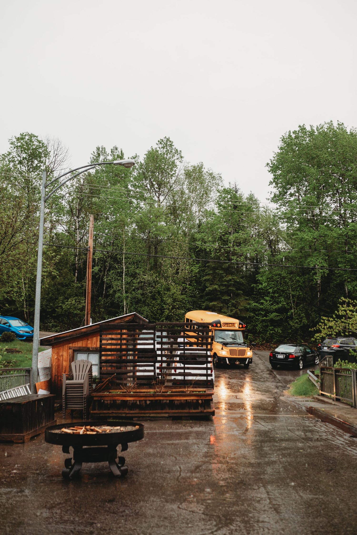 Rainy day at venue with yellow school bus parked near wooden deck and green forest background.