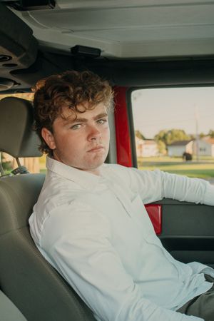 Person sitting in car wearing white button-down shirt and looking to side.