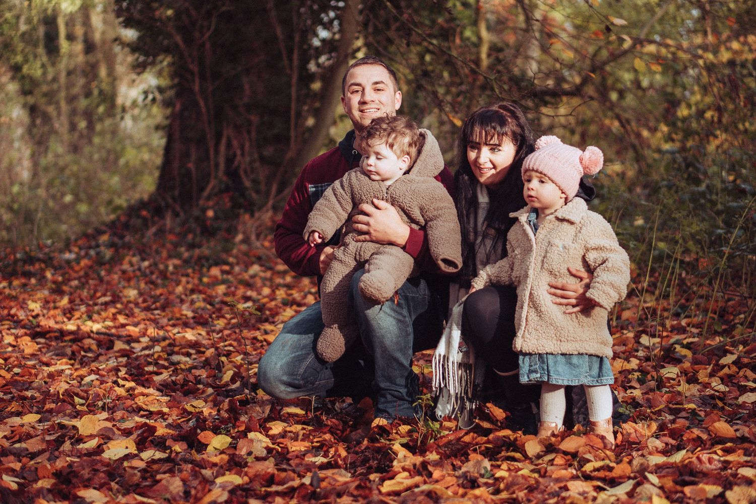 Young family crouched down in the autumnal leaves, orange and brown.