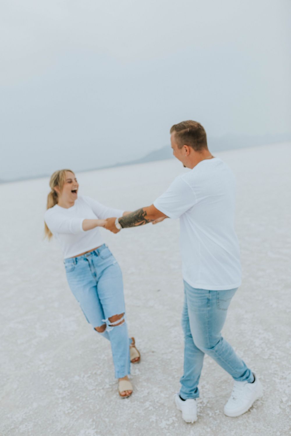 A couple laughs during their summer engagement session at the Utah Salt Flats.