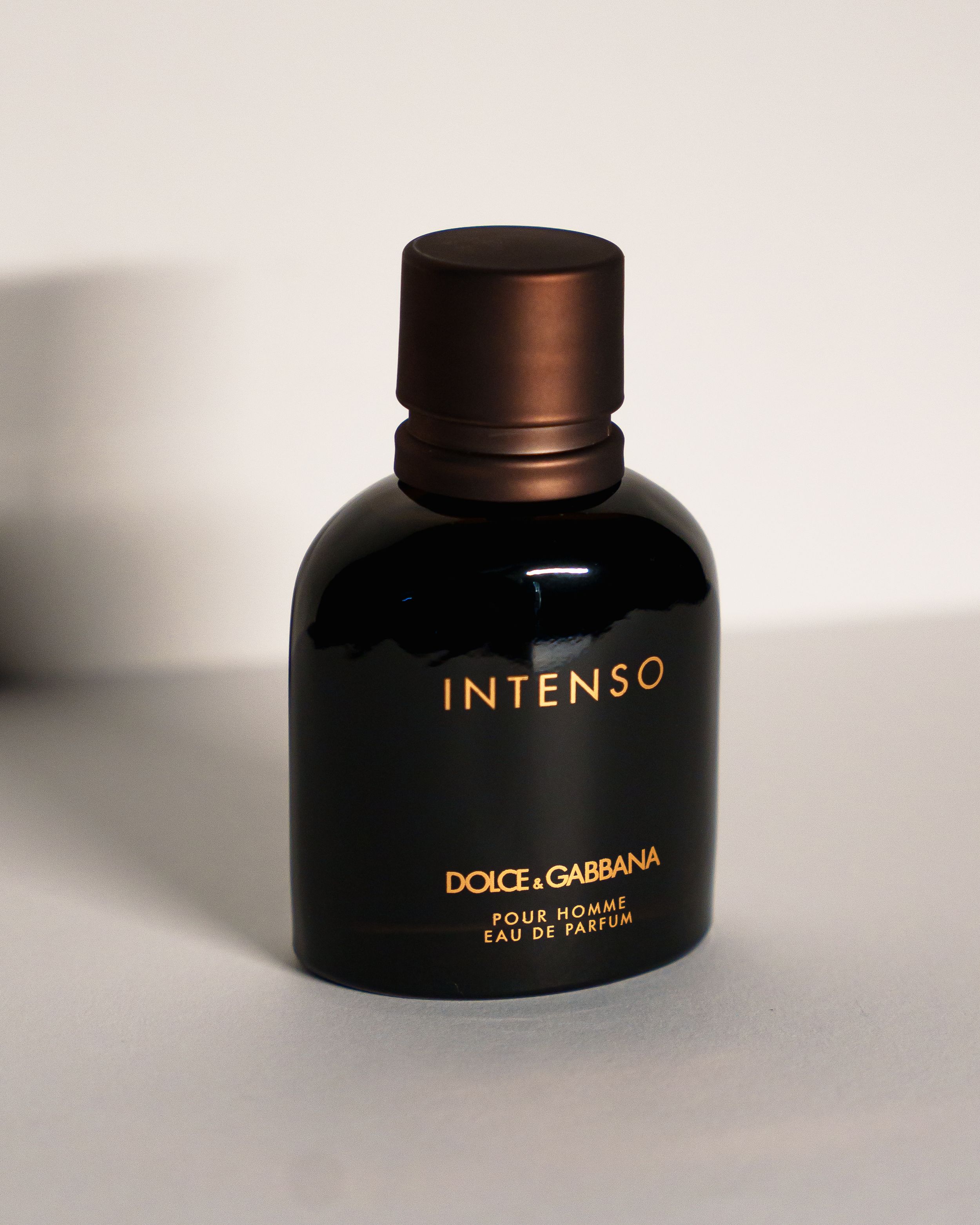 A black glass bottle of Dolce & Gabbana Intenso eau de parfum against a neutral background.