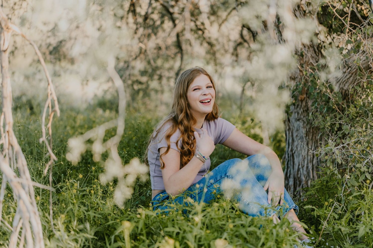 Young woman in blue dress sitting among wildflowers in dreamy natural setting.