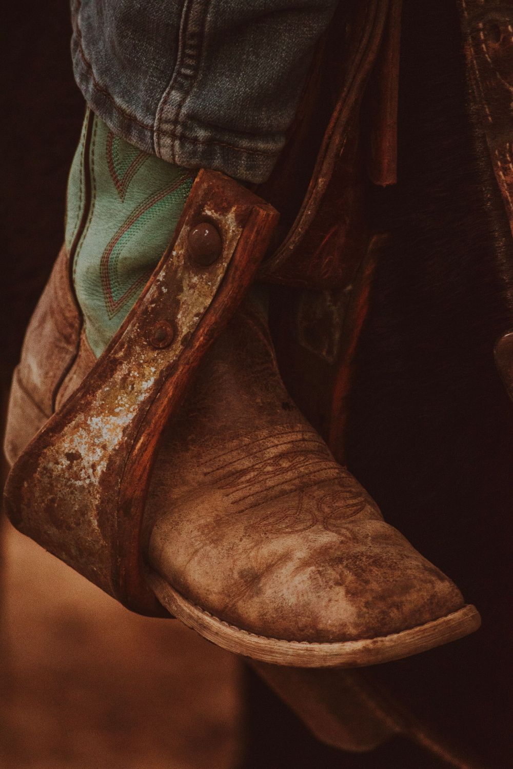 Close-up of a worn leather cowboy boot with turquoise details against a dark background.