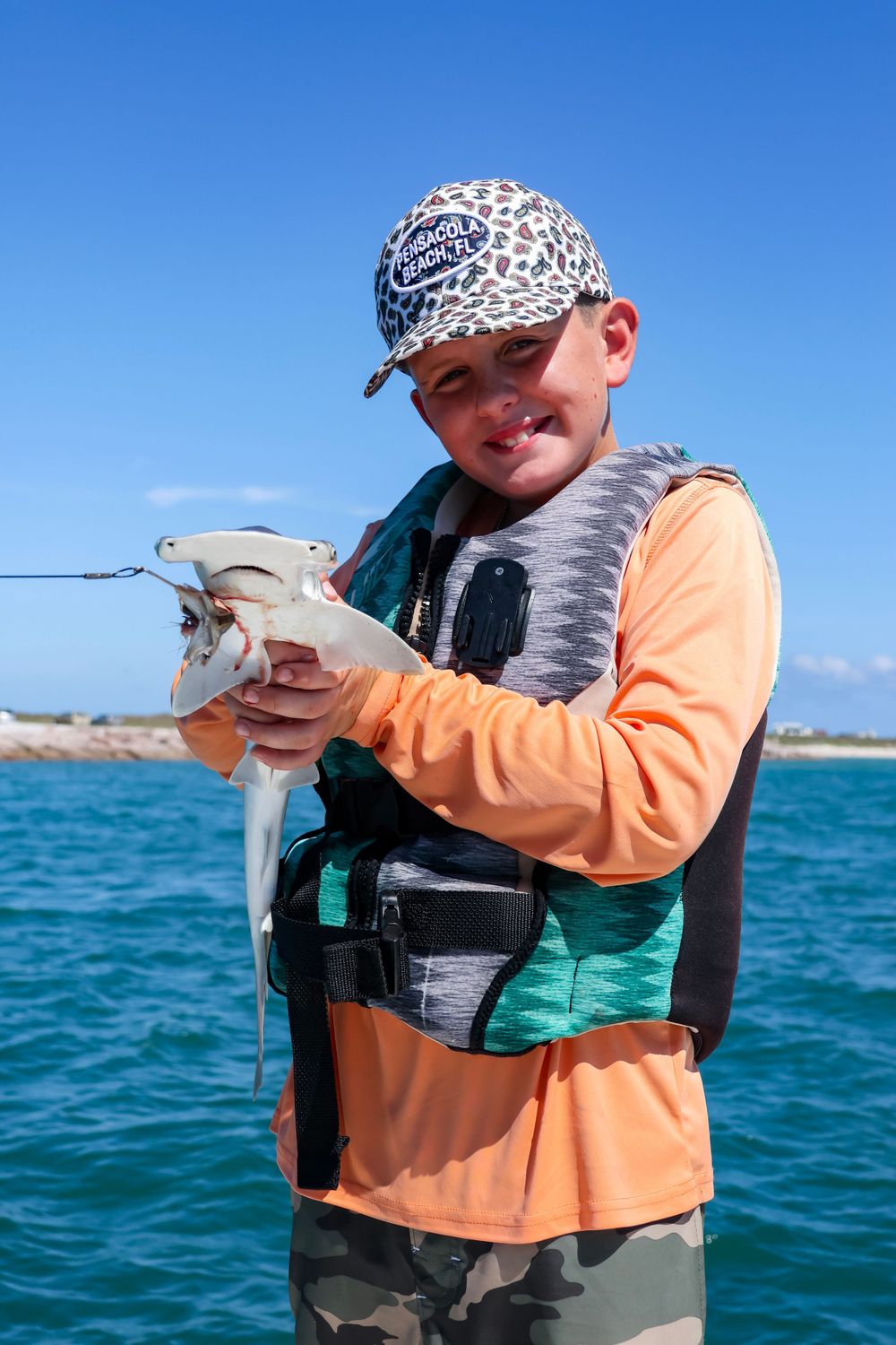 Angler wearing orange and camo gear shows off fresh catch on boat in coastal waters.