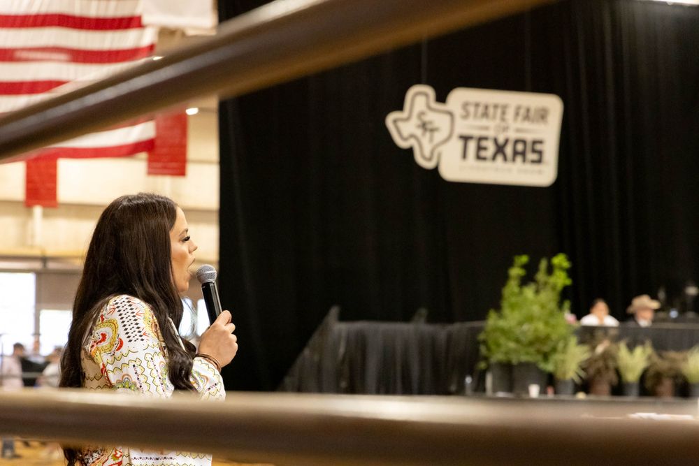 A speaker presents at the Texas State Fair with stage and banner visible.