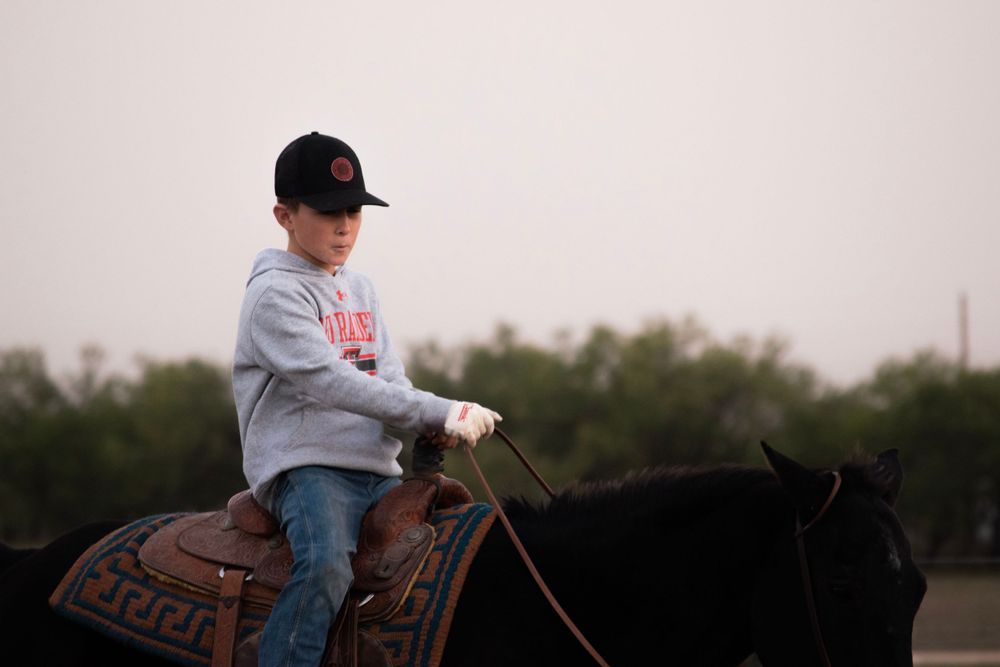 A young rider sits atop a dark horse in evening light.