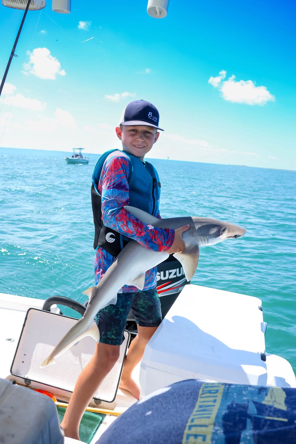 Young angler proudly displays a fish catch on a boat during a sunny day on bright blue waters.