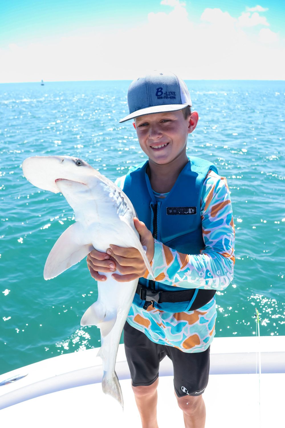 Catch of the day being shown off on a white boat deck against sparkling turquoise ocean waters.