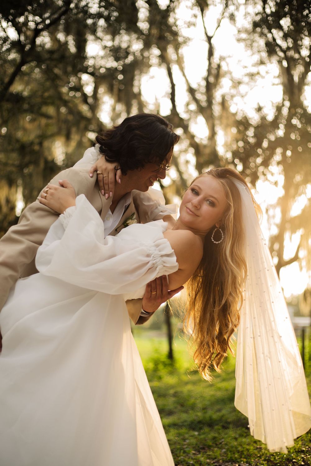Romantic wedding couple embraces in a dreamy forest setting with golden sunlight filtering through Spanish moss.