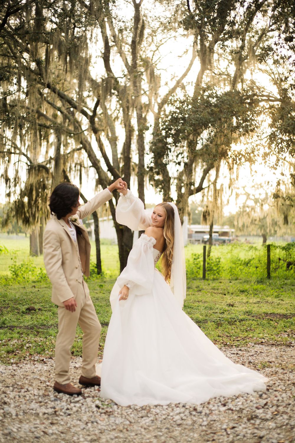 Wedding couple dances playfully on a gravel path beneath Spanish moss-covered trees.
