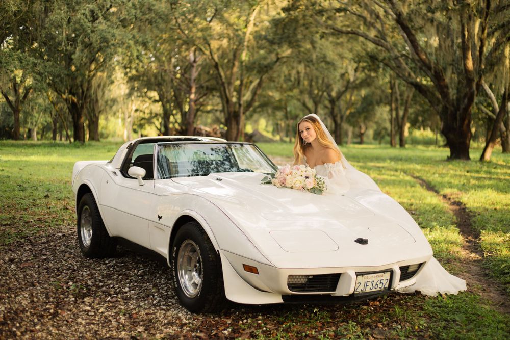 Classic white Corvette parked under moss-covered trees serves as elegant wedding photo backdrop.