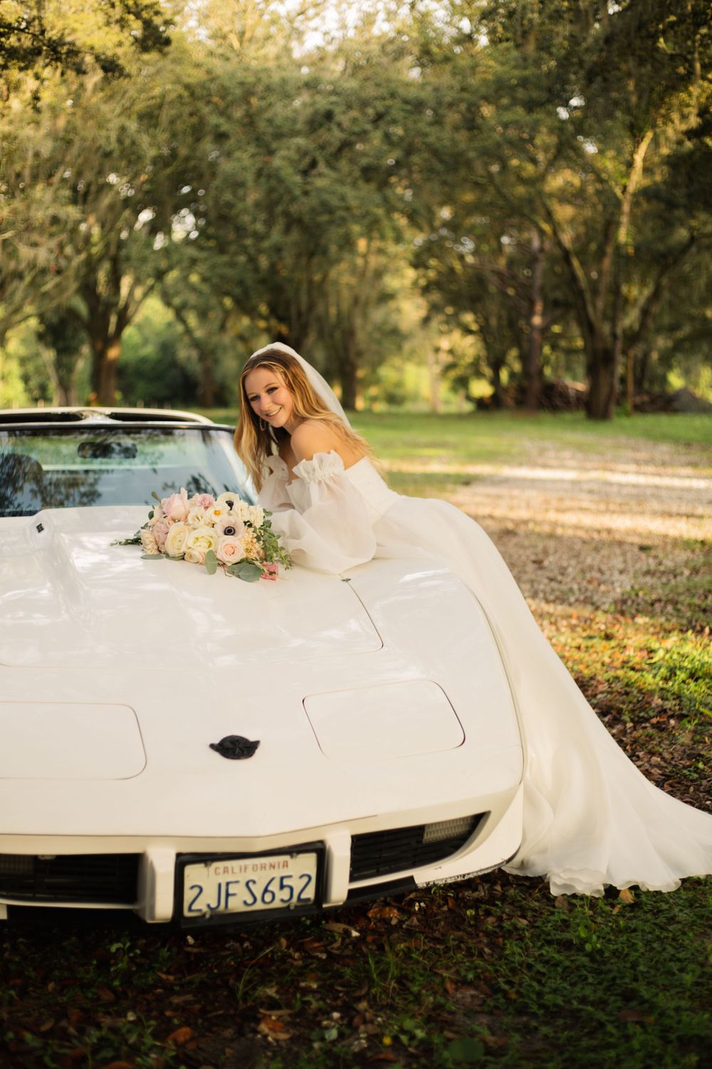 A white wedding dress flows over a classic Corvette surrounded by Spanish moss draped trees.