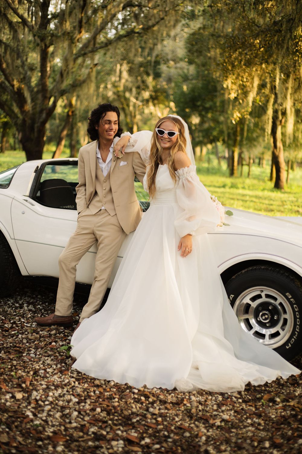Stylish wedding photo featuring sunglasses and a white Corvette under moss-draped oaks.