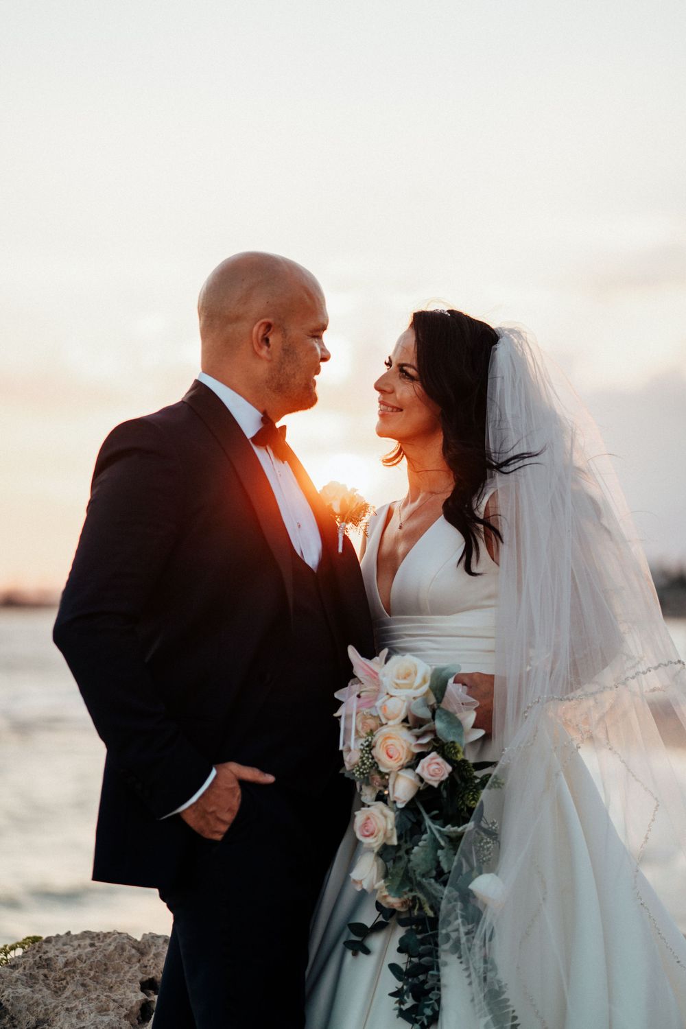 A wedding couple shares a tender moment at sunset by the ocean.