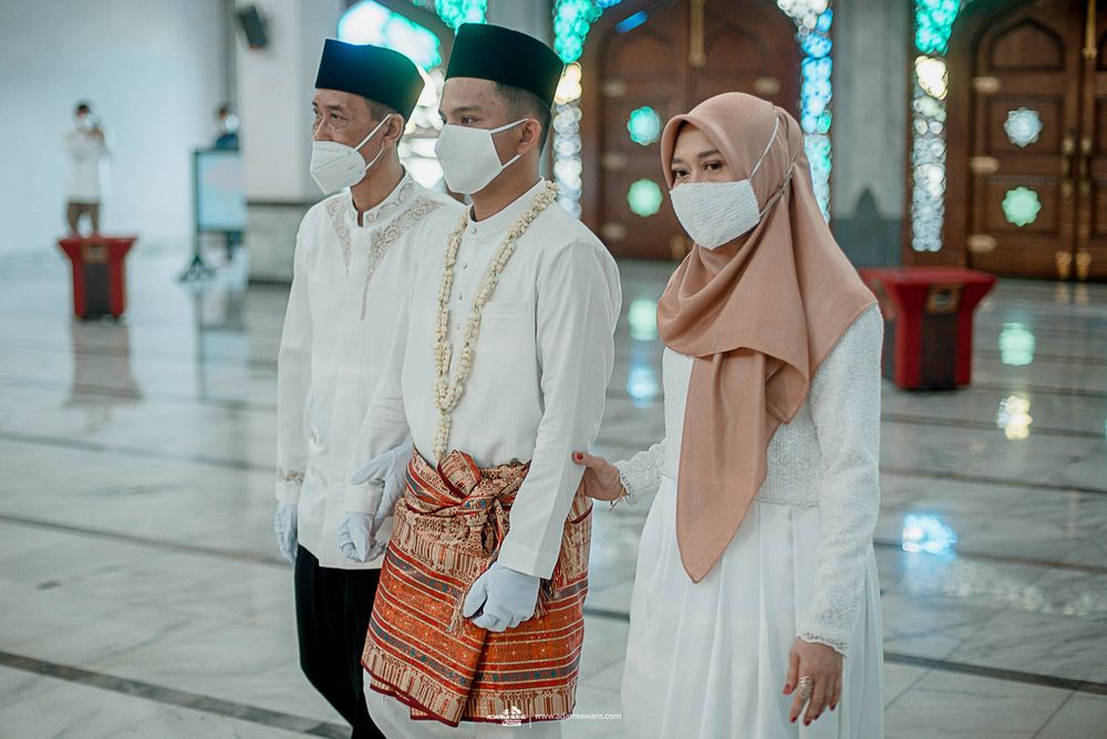 Three people in white and beige attire stand together inside a mosque.