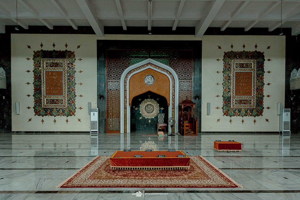 Interior of mosque with ornate archway and red prayer rug on marble floor.