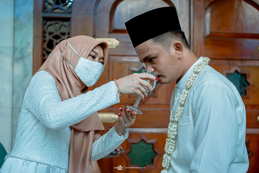 A couple in traditional Muslim attire performs a ceremonial ritual during a wedding ceremony.
