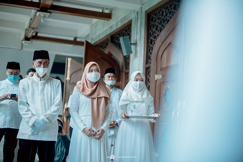 People in white traditional clothing and masks gathered in hallway.
