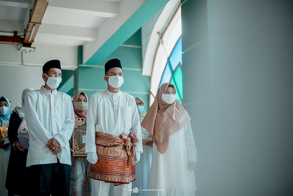 Group in traditional Muslim attire standing against turquoise wall.