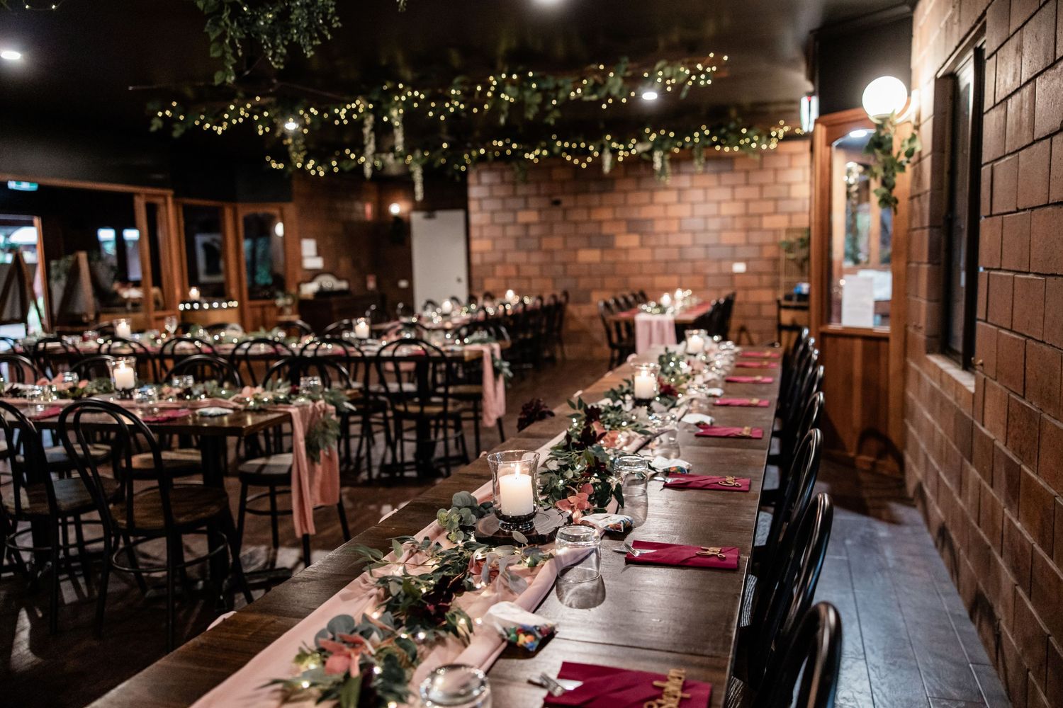 Elegant wedding reception venue with brick walls, string lights and burgundy table settings.