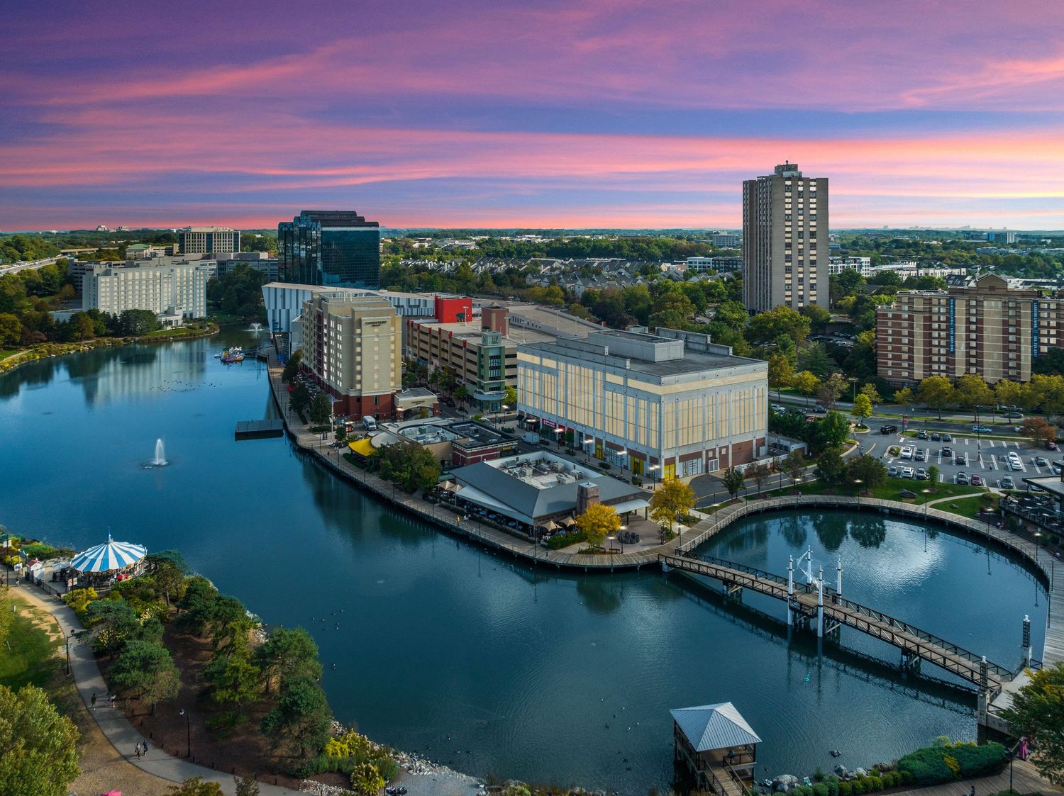 Twilight aerial view of waterfront buildings and bridges with pink and purple sky reflections.