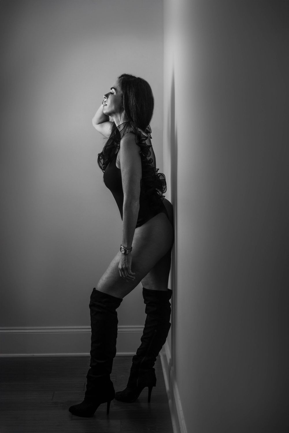 Black and white boudoir portrait of a woman in luxurious lingerie and tall boots, showcasing confidence and femininity.