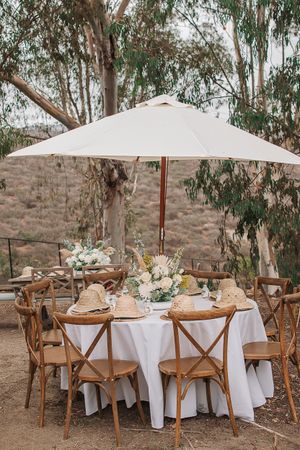 Outdoor event setup with wooden chairs and white tablecloths under eucalyptus trees.