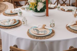 Table settings with white linens, woven placemats, and blue accent plates at an outdoor venue.