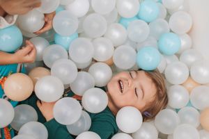A joyful moment captured of someone playing in a ball pit filled with white and blue spheres.