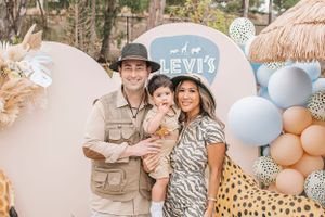 An outdoor celebration with balloon decorations and people posing together under a safari-themed setting.