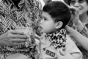 Black and white image of a young child in a leopard print scarf drinking from a glass at a party.