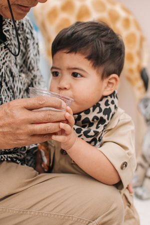 Close-up of small child in safari outfit drinking from glass with giraffe print backdrop.