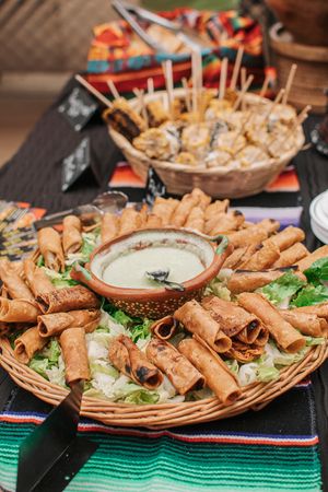Platter of crispy spring rolls served with dipping sauce on colorful striped tablecloth.