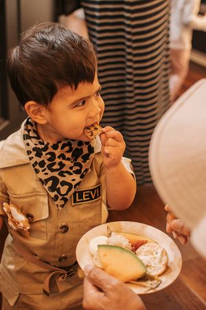Child in safari outfit with leopard print bandana enjoying party snacks.