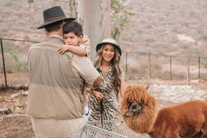 Family interacting with brown and white llamas at an outdoor animal enclosure.